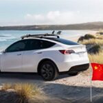 Tesla Model Y sulla spiaggia e in basso a destra una bandiera cinese