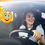 Una donna al volante di un'auto e a sinistra un emoticon con il pollice su