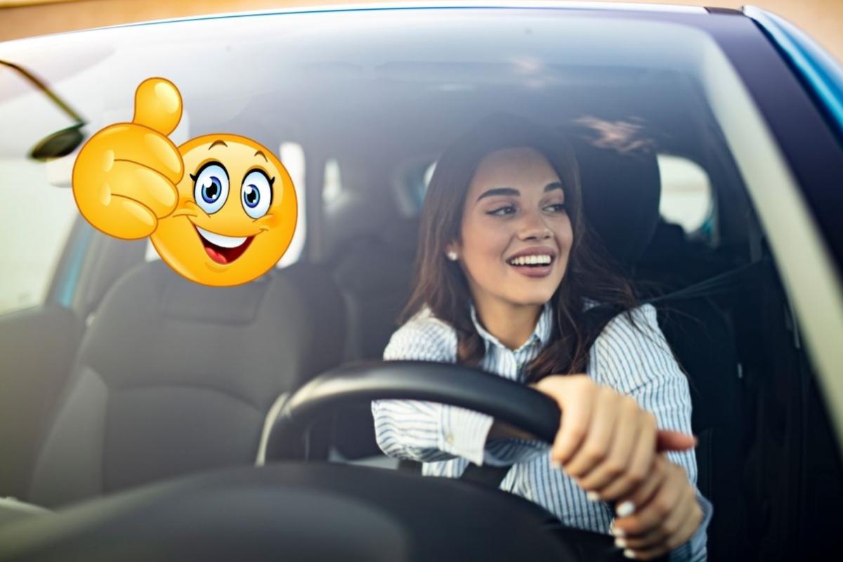 Una donna al volante di un'auto e a sinistra un emoticon con il pollice su