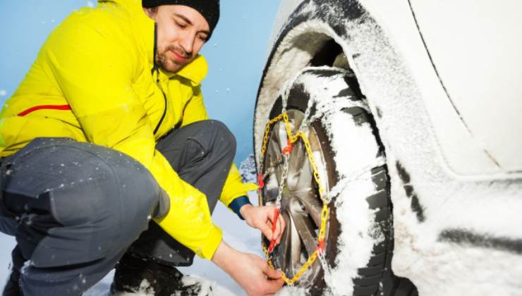 Uomo monta le catene sulle gomme della sua auto nella neve