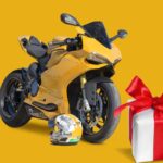 Una moto gialla con il casco appoggiato a terra e a destra il disegno di un pacco regalo