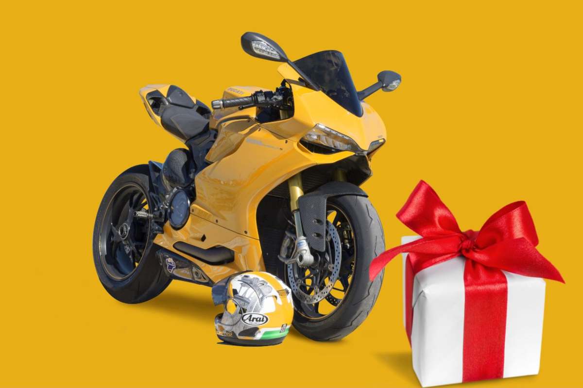 Una moto gialla con il casco appoggiato a terra e a destra il disegno di un pacco regalo