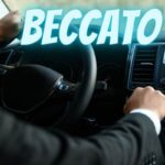 Un uomo guida un'auto e la scritta "Beccato"