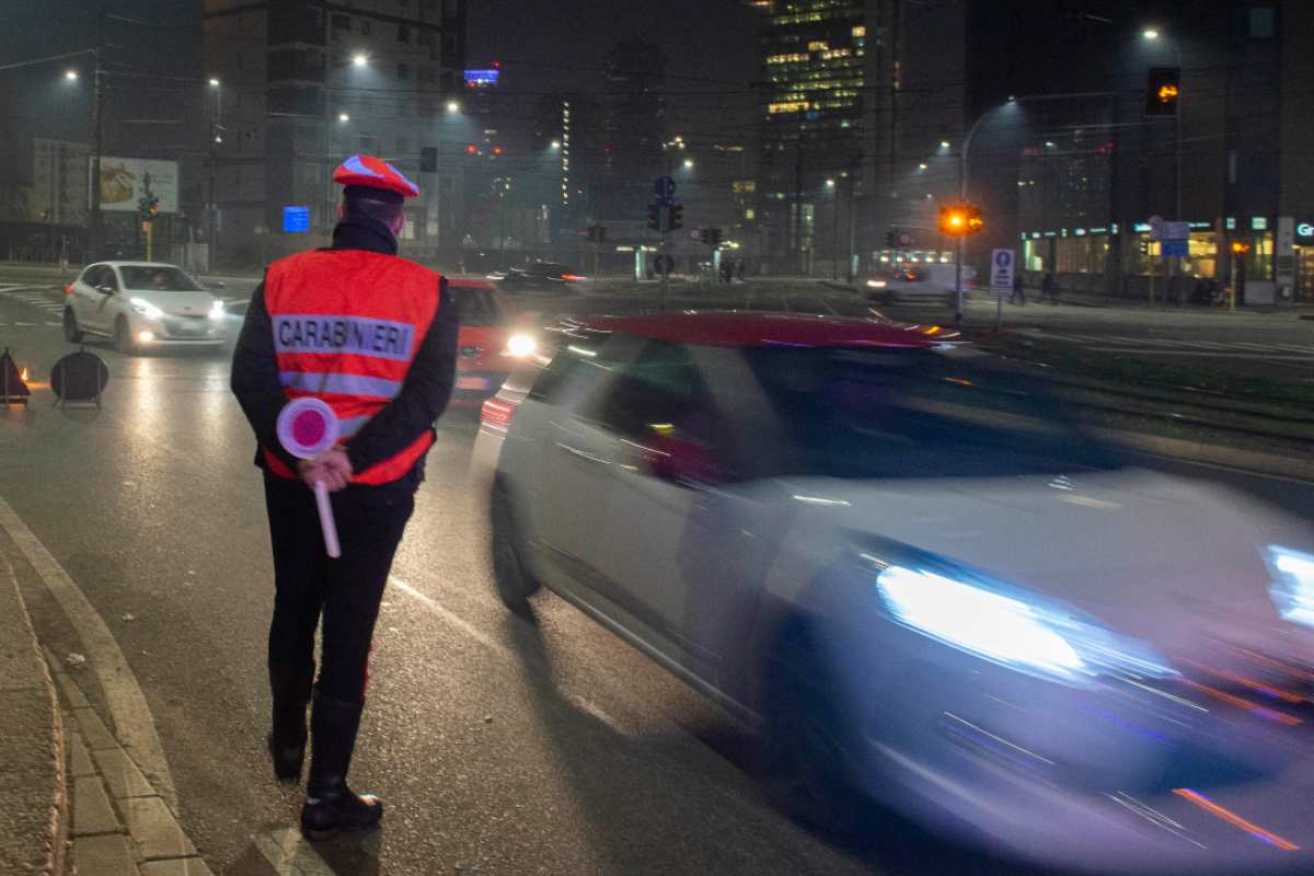 Un carabiniere a bordo strada e una macchina di passaggio