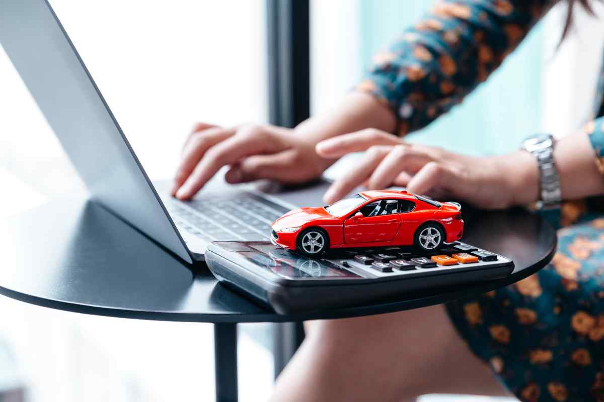 Persona al computer con modellino di auto e calcolatrice